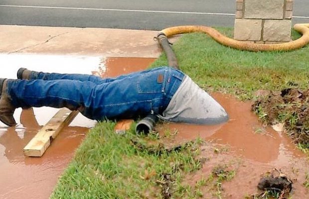 man in mud water fixing pipe